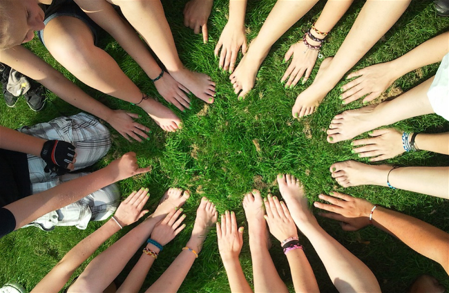 Picture of grass with people's hands and feet making a circle, indicating community building